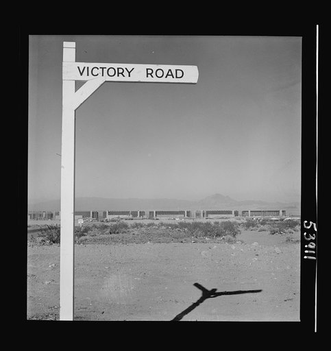 Untitled photo, possibly related to: Las Vegas, Nevada. A crossroad sign reading "Victory Road," with buildings, storage silos and transmission lines of the Basic Magnesium Incorporated plant in the background