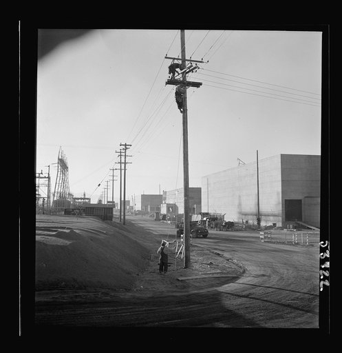 Untitled photo, possibly related to: Las Vegas, Nevada. A view of the plant of Basic Magnesium Incorporated, showing unfinished roads, power lines, telephone lines on which two men are working, and buildings during an early stage of construction