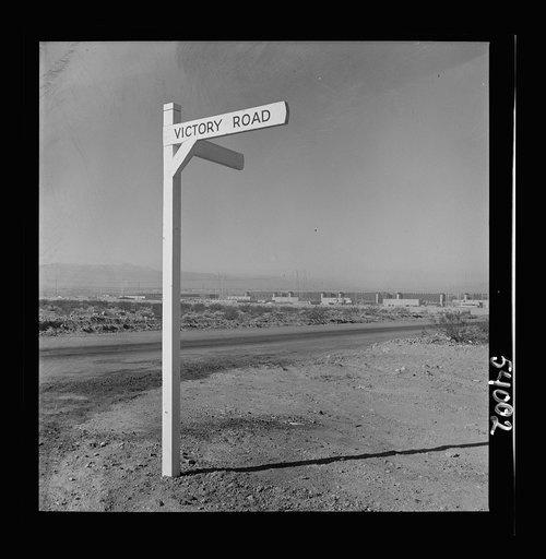 Untitled photo, possibly related to: Las Vegas, Nevada. A crossroad sign reading "Victory Road," with buildings, storage silos and transmission lines of the Basic Magnesium Incorporated plant in the background