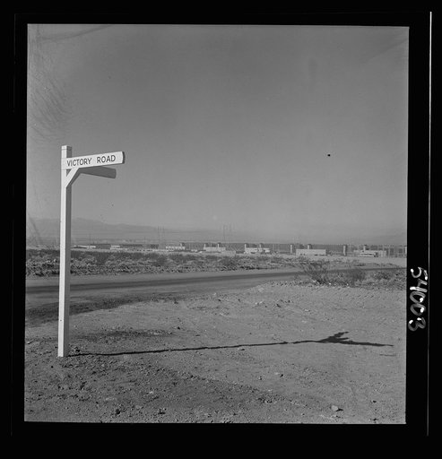 Untitled photo, possibly related to: Las Vegas, Nevada. A crossroad sign reading "Victory Road," with buildings, storage silos and transmission lines of the Basic Magnesium Incorporated plant in the background