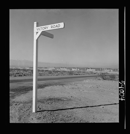 Untitled photo, possibly related to: Las Vegas, Nevada. A crossroad sign reading "Victory Road," with buildings, storage silos and transmission lines of the Basic Magnesium Incorporated plant in the background