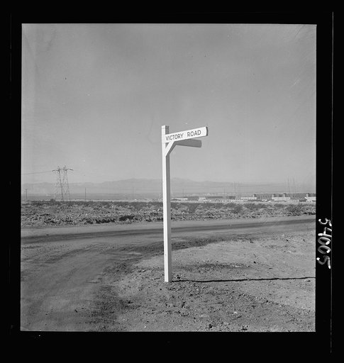 Untitled photo, possibly related to: Las Vegas, Nevada. A crossroad sign reading "Victory Road," with buildings, storage silos and transmission lines of the Basic Magnesium Incorporated plant in the background
