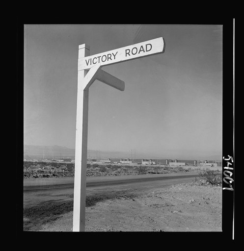 Untitled photo, possibly related to: Las Vegas, Nevada. A crossroad sign reading "Victory Road," with buildings, storage silos and transmission lines of the Basic Magnesium Incorporated plant in the background