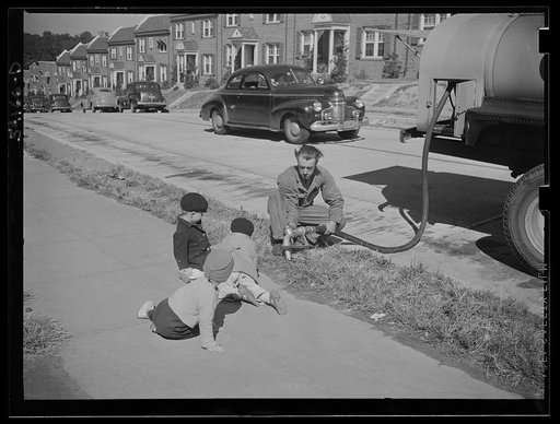 Washington, D.C. A fuel-oil truck driver filling a tank at a residence. Three small boys fascinated with the operation are sprawled on the sidewalk beside him