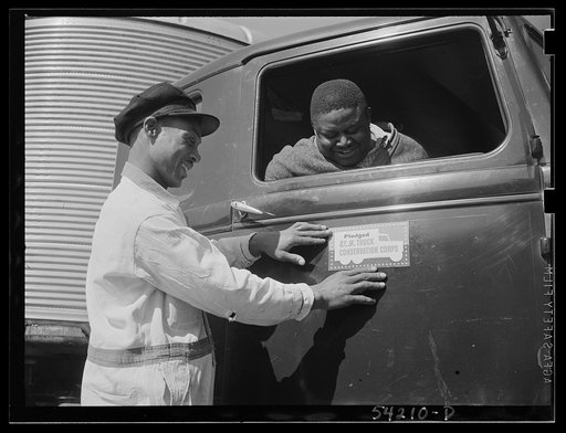 Untitled photo, possibly related to: Washington, D.C. A colored driver on the running board of an autocar van giving some directions to someone ahead. A pledge to the United States Truck Conservation Corps is displayed on the door of the car