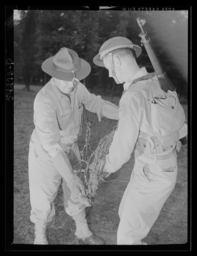 Fort Belvoir, Virginia. Two soldiers, wearing heavy gloves, handling barbed wire steel screw type picket