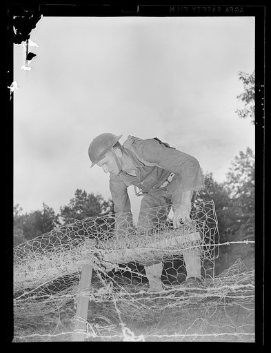 Fort Belvoir, Virginia. A soldier unrolling fence wire over a barbed wire steel screw type picket
