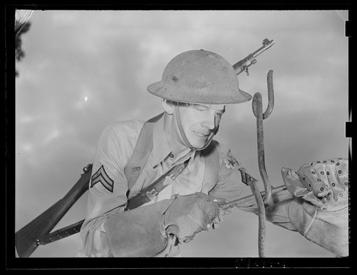 Fort Belvoir, Virginia. A soldier using a barbed wire anchor spike to screw in a picket. He is wearing special gloves that are made for handling barbed wire