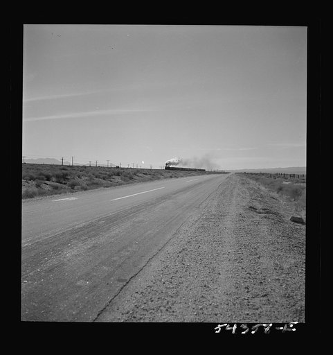 Kingman (vicinity), Arizona. A road passing close to the recovery plant where the tungsten ore from the Boriana mine workings, is processed. A transcontinental railroad train is running parallel to the road