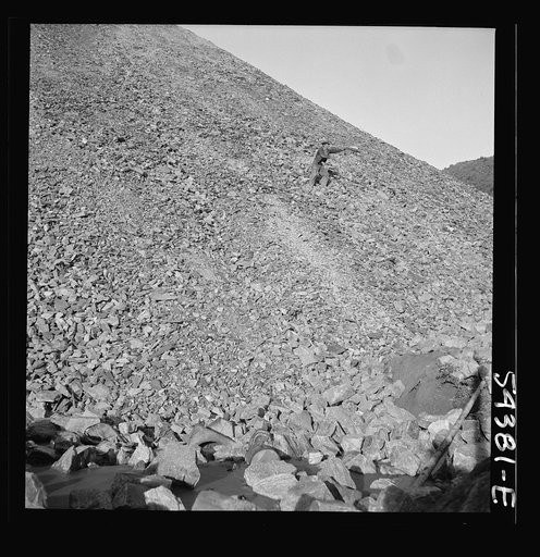 Kingman (vicinity), Arizona. A huge waste pile, showing a workman near the center picking up still valuable pieces of tungsten ore, which is mined at the Boriana workings and processed at a nearby recovery plant