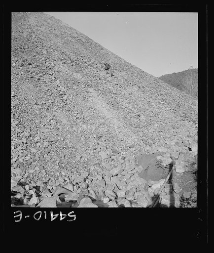 Untitled photo, possibly related to: Kingman (vicinity), Arizona. A huge waste pile, showing a workman near the center picking up still valuable pieces of tungsten ore, which is mined at the Boriana workings and processed at a nearby recovery plant