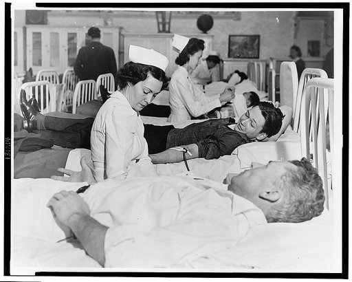 A prisoner gives blood for America's fighting men while another watches with interest. The Red Cross mobile unit makes periodic visits to San Quentin and other institutions where residents wish to make this contribution to victory