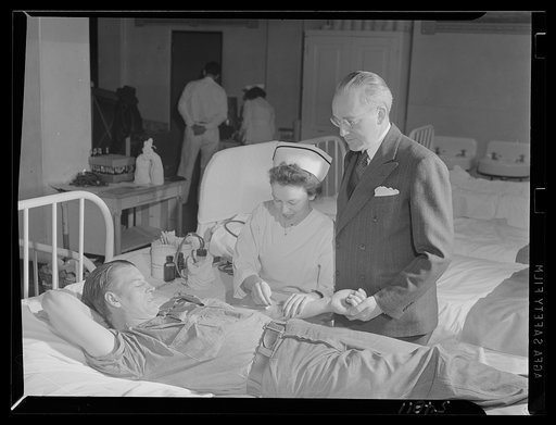 Clinton D. Duffy, warden of San Quentin, stands at a prisoner's bedside while Red Cross nurse Florence Aldrich prepares trhe young man for his donation. During the Red Cross mobile unit's visit, 150 men gave blood to the bank and more than twice that number volunteered but could not give because of 