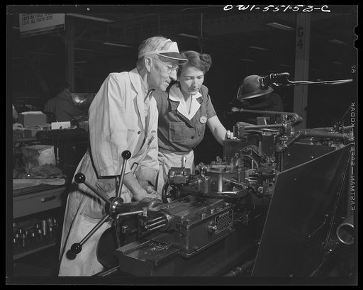 Skilled machinists are vital to the war production program. Here a woman employee operates a turret lathe under the close supervision of a skilled machinist in North American's modern machine shop