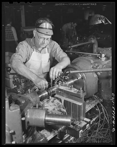 A skilled machinist on a turret lathe in North America's machine shop tests the accuracy of his work with a micrometer