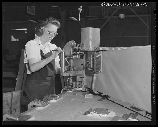 In the material preparation department, this woman employee uses a router to drill holes in a dozen sheets of metal at once with a master template