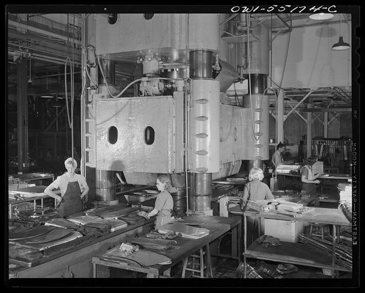 This huge hydropress is operated day and night by women employees. Thousands of sheet metal parts are formed daily on this press. Worked from four sides using same die. Beds with metal to be shaped is rolled into place under hydraulic press. 3000 tons total pressure