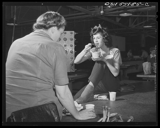 Two women "swing shift" employees at North American "talk over" the day's events as they eat lunch at their benches. The company broadcasts news and music throughout the plant during lunch periods