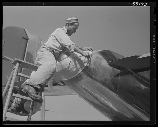 The tail cone of a North American B-25 bomber is masked off by a painter before the ship receives its camouflage. Cone contains tail and signal light. No more gunners