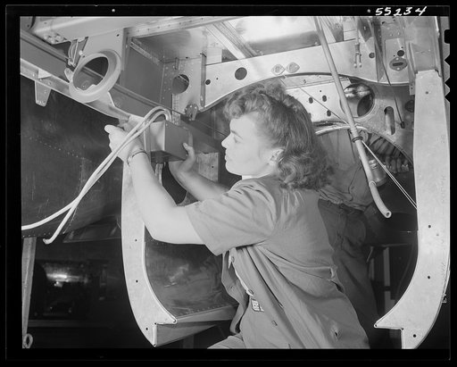 Inside the fuselage of a North American P-51 fighter, this woman employee assembles an electrical switch box