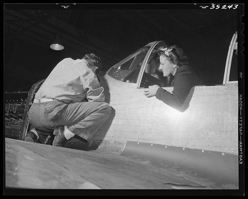 On the final assembly line at North American Aviation, men and women work together adjusting the controls of P-51 Mustang fighters for the United States Army Air Forces