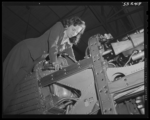A woman employee on the P-51 Mustang fighter assembly line at North American Aviation adjusts the engine controls before the plane moves down the assembly floor