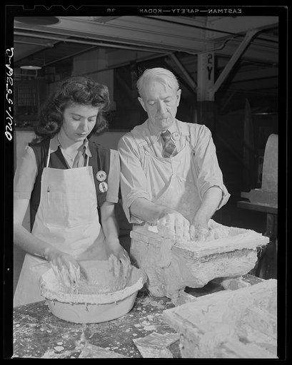 This woman employee mixes plaster to the right consistency as a master at plaster forming makes a mould for a new die