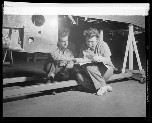 A man and woman employee on North American's P-51 fighter final assembly line check their day's work on a "sign-off" sheet as each assembly is completed