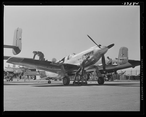 Painters swarm over a North American P-51 fighter as it leaves the assembly line. Cleaning before spray painting