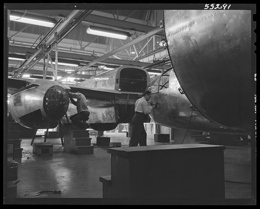 North American B-25 bomber fuselage sections move down a long overhead powered conveyor belt