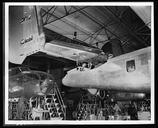 The tail assembly for a North American B-25 bomber is lowered into place from an overhead crane on the final assembly floor