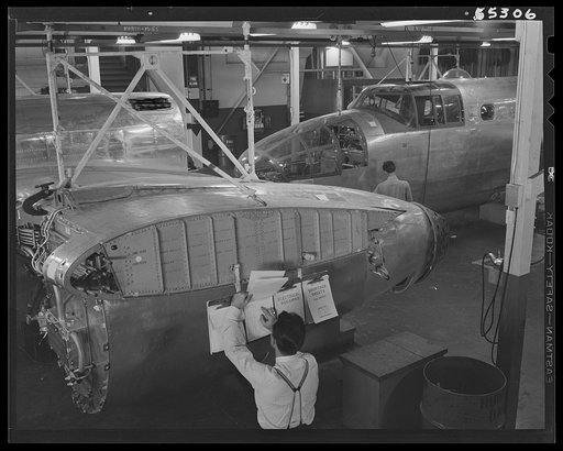 North American B-25 bomber fuselage sections move down a long overhead powered conveyor line