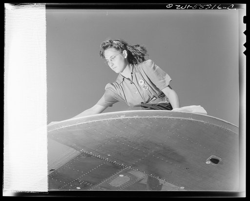 The wing is a North American B-25 is prepared for painting on the "California Assembly Line." The girl is taping down strips of paper to protect areas not to be painted