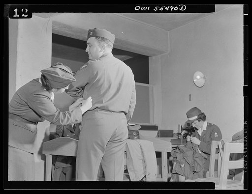 Catching that stitch in time, Mrs. Viola Schlaegel of the American Women's Volunteer Service unit at Glendale, California does a good turn for Corporal Hugh B. Helm of Lexington, Kentucky. Members of the American Women's Volunteer Service "Button Brigade" meet at least twice weekly at the Army Air F