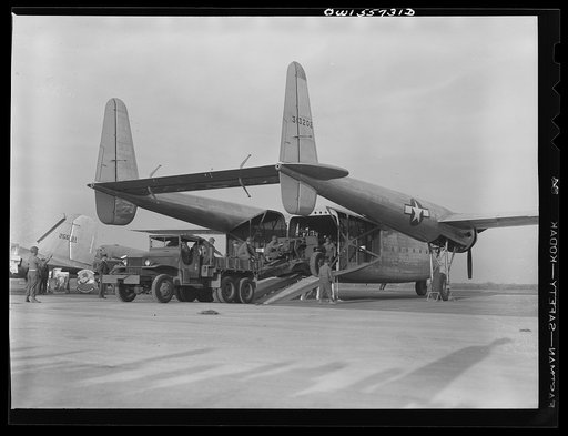 Howitzer being loaded into the new C-82 at demonstration of equipment held by United States Army Air Forces. The specific function of this plane is to land heavy military loads safely on rough fields near battle points. Note twin boom tail. Plane has wing span of 106 feet, and carries tricycle landi