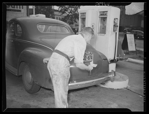 Gas station attendant checking ration coupons against license plate of Washington, D.C. Dodge automobile. Sign on sidewalk reads "Today's quota sold"