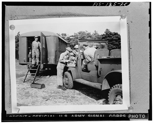 An army truck being repaired at a mobile unit in England. Note the caution sign on this American vehicle from a "keep to the right" country, now in a "keep to the left" one