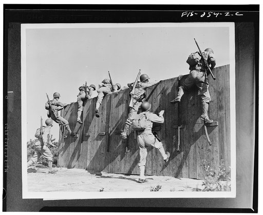 Camp Edwards, Massachusetts. Up and over an eight-foot wall go seven soldiers of the anti-aircraft training center. The ropes are used only by the shorter warriors who cannot otherwise reach the top. Note the full equipment on each soldier