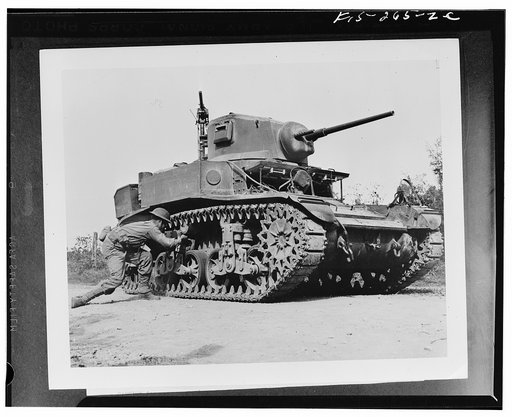 Sergeant Carl Hardy, twenty, of Shelby, North Carolina, stalking a tank on maneuvers with the Second Army in middle Tennessee. The simulated twenty-nine pound TNT statchel charge laid on the bogey of the light tank will "wreck" it, and possibly "kill" the four operators within