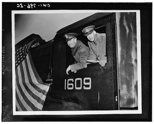 Colonel N.A. Ryan, acting chief of transportation, U.S. Army European theater of operations, and Major General D.J. McMullen, D.S.O., C.B.E., director of transportation, British Army, leaning out of the locomotive which was among the first of a shipment to arrive in Great Britain. Small in compariso