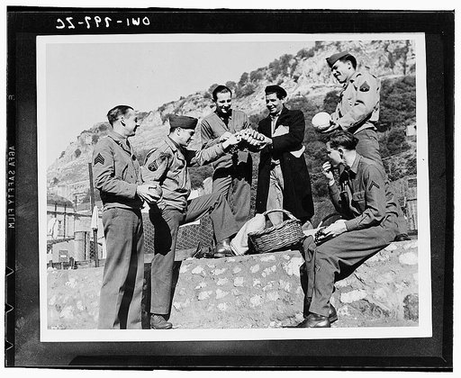 American troops in North Africa sample the wares of a fruit vendor. Left to right: Sergeant Hardy Patillo of Austin, Texas; Captain Louis Dubcak of Lexington, Texas; Sergeant Adan Garza of Laredo, Texas; and Private First Class Herbert Lipsey of Dade City, Florida