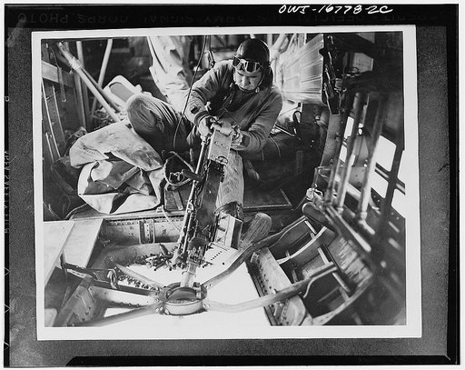 United States Army air force gunner Sergeant William Watts of Alexandria, Louisiana, training machine gun on the enemy during a aerial fight with German planes somewhere in the European war theater. Behind him may be seen the legs of another gunner operating his weapon from the side of the plane