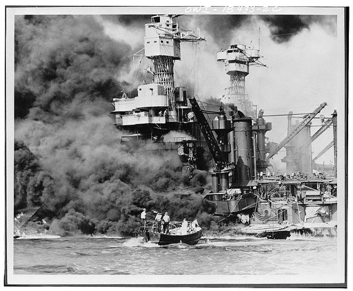 Pearl Harbor, Hawaii. A small boat rescues a seaman from the 31,800 ton USS West Virginia burning in the foreground. Smoke rolling out amidships shows where the most extensive damage occurred. Note the two men in the superstructure. The USS Tennessee is inboard