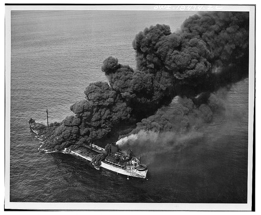 A United States tanker torpedoed by an Axis submarine. Despite a raging fire which sent columns of black, oily smoke billowing into the sky, crew members were able to bring the flames under control and the tanker was towed to port by a United States Naval ship. The tanker is now in an east coast shi