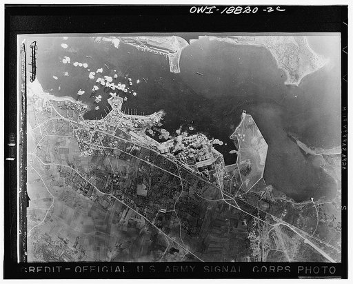 Bizerte, Tunisia. Bursts of bombs from a Flying Fortress exploding at the Bizerte naval base held by the Axis. Not only was shipping struck but great damage was done to shops and oil tanks along the coast line