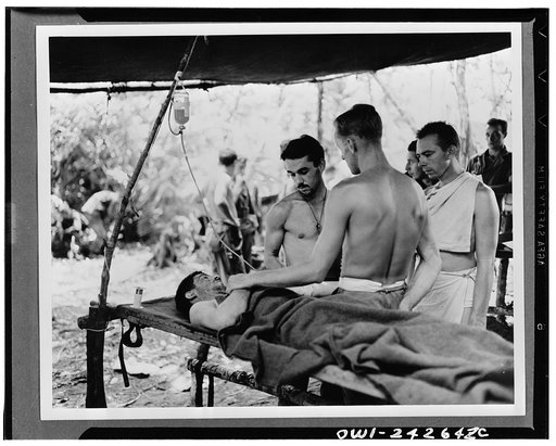 Administering blood plasma to a wounded soldier at the portable hospital in New Guinea. Clayton Mitchell of Wyandotte, Michigan, and Major William Garlick of Baltimore, Maryland, are administering