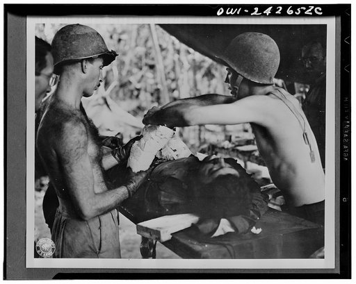 An operation on wounded American soldier is performed by Major George Marks. The soldier has been wounded in the arms and shoulders by shrapnel from a Jap mortar as he was storming a pillbox in New Guinea