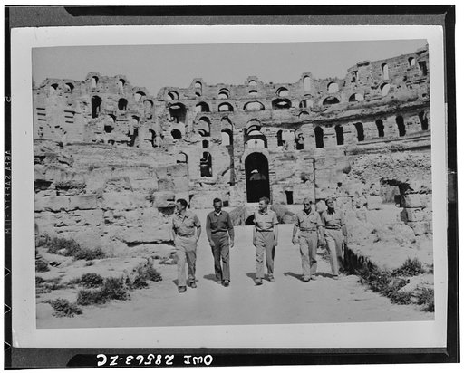 Officers of the 57th Fighter group United States Army Air Force, look over the ruins of a Roman coliseum in Tunisia. These are a few of our airmen who knocked Nazi planes out of the skies above Sicily Straits and are now getting their birdeye's of Italy, itself