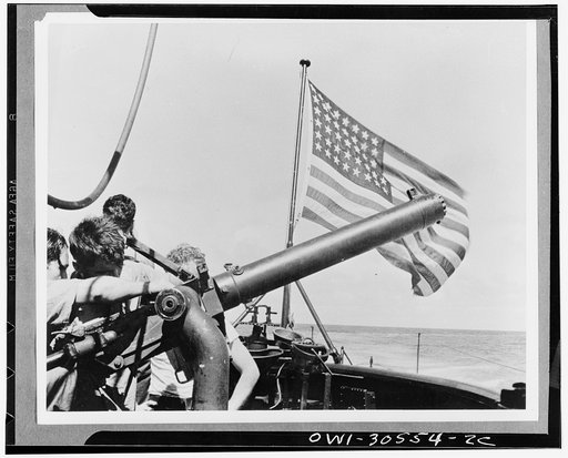 Ready for trouble from the conning tower of the United States submarine. A crew swings a fifty caliber machine gun skyward to safeguard the underseas craft against a possible surprise air attack. Submarine rarely comes to surface during daylight hours. The man in the left background is scanning the 