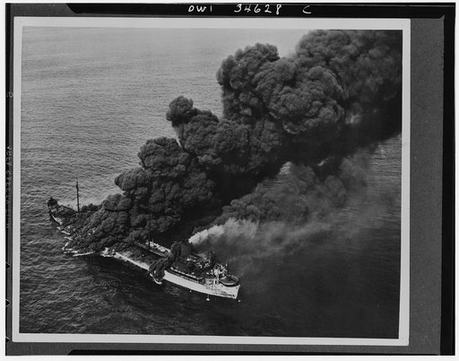 A U.S. tanker torpedoed by an Axis submarine. Despite a raging fire which sent columns of black oily smoke billowing into the sky, crew members were able to bring the flames under control, and the tanker was towed to port by a U.S. naval ship